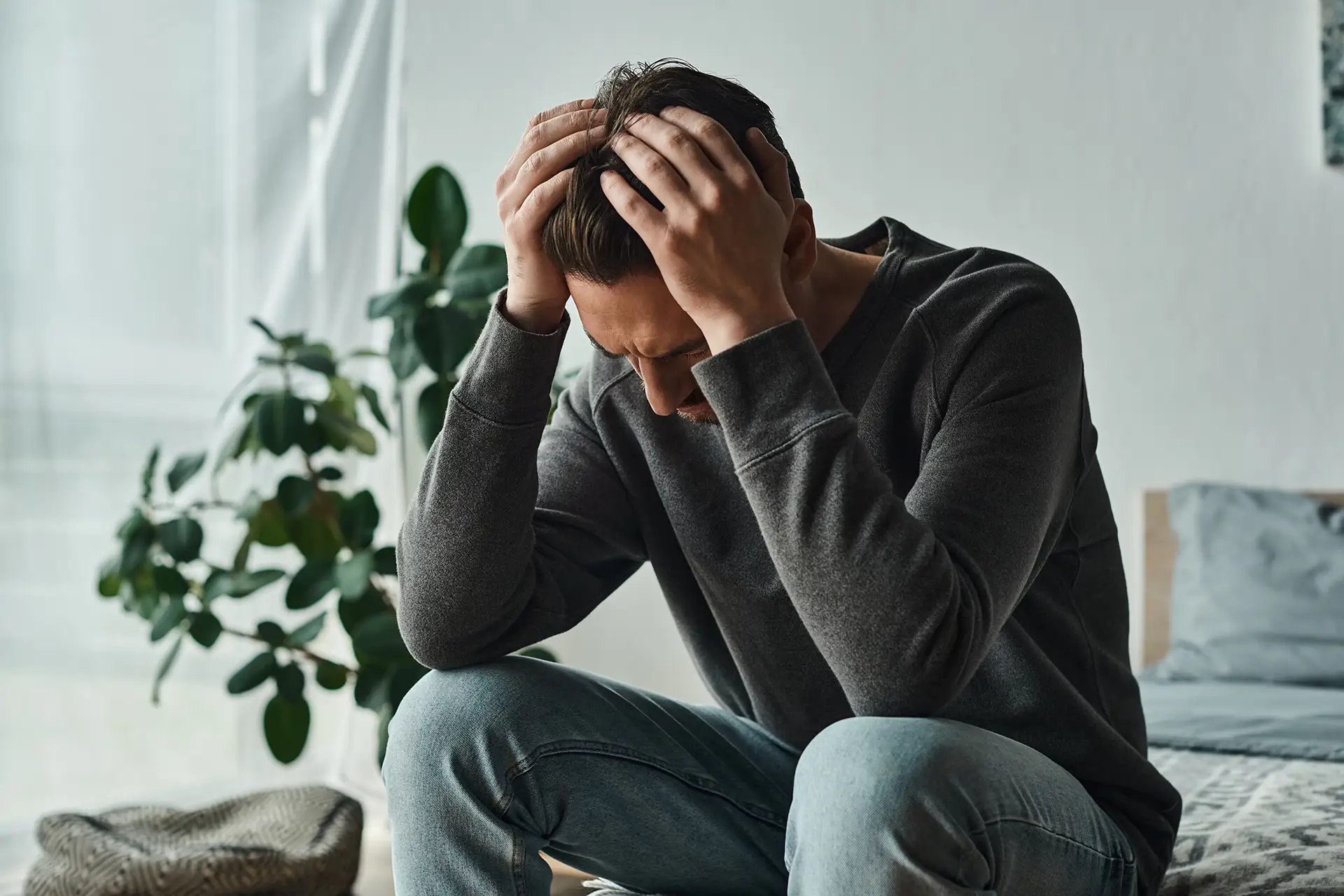upset bearded man in casual home wear touching head while sitting on bed at home,